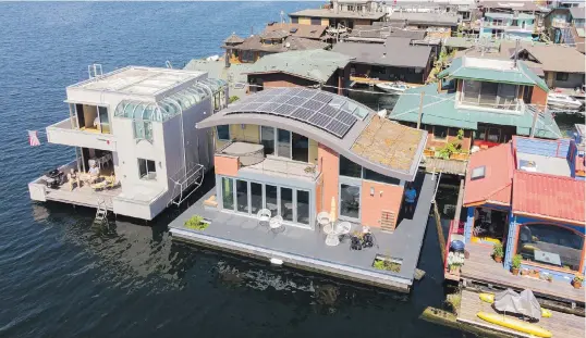  ??  ?? Architect Michelle Lanker, her husband, Bill Bloxom, and dogs Bing and Arnie live on the second floating home from the left — the one with the distinctiv­e curved roofline, solar panels and vegetated roof system. G. Little Constructi­on built the LEED Platinum-certified home in Port Townsend, Washington, before it was towed to Lake Union.