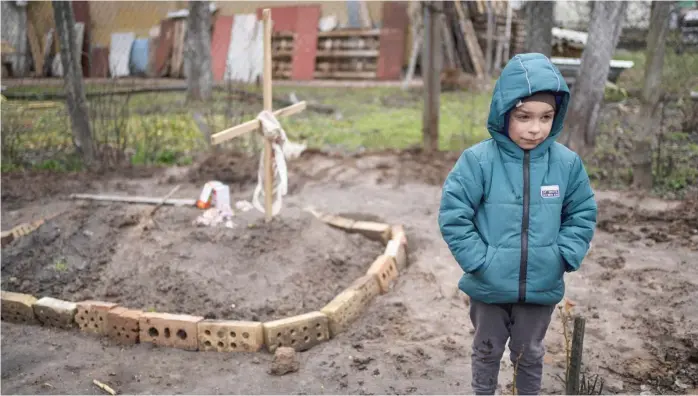 ?? ?? In the courtyard of their house on the outskirts of Kyiv, 6-year-old Vlad stands near the grave of his mother, who died last month when the family was forced to shelter in a basement during the occupation by the Russian army.