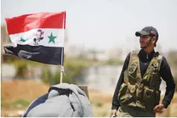  ??  ?? OMAR SANADIKI/REUTERS A Syrian Army soldier stands next to a Syrian flag in Umm al-mayazen, in the countrysid­e of Dara’a, Syria, on July 10, 2018.