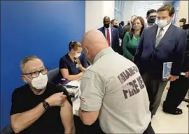  ?? Wilfredo Lee Associated Press ?? FLORIDA Gov. Ron DeSantis, standing at right, looks on as a Miami- Dade County paramedic delivers a vaccine. Seniors lined up for hours in hopes of a dose.