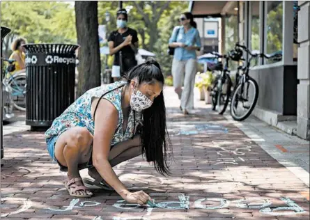  ?? BRIAN CASSELLA/CHICAGO TRIBUNE ?? Ashbey Beasley works on anti-racist chalk messages, one of many left by North Shore residents, on a sidewalk on Thursday in Glencoe.