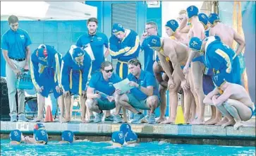  ?? Minette Rubin ?? MEMBERS of the UCLA water polo team gather around coach Adam Wright, shown with a document, during a recent match against Stanford. As a student, Wright won titles in his final two years with the Bruins.