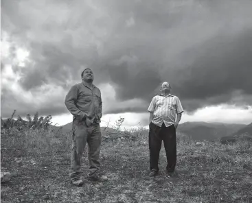  ?? Associated Press ?? ■ Retired resident Ramon Serrano, right, stands outside his home with a lineman from the Puerto Rico Power Authority as they watch a man restore power that was cut off by hurricanes Irma and Maria in Adjuntas, Puerto Rico. For the first time in 10...
