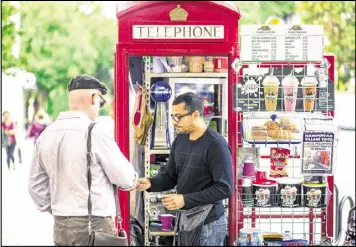  ?? MILES WILLIS / BLOOMBERG ?? Umar Khalid, co-owner of the Kape Barako telephone box coffee stall, serves a customer on Hampstead High Street in London.