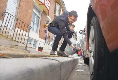  ?? LLOYD FOX/BALTIMORE SUN ?? Eli Pousson picks up trash as he walks his daughters to school each morning, challengin­g Marylander­s to pick up trash every day in April. His daughter Naomi watches as he picks up a soda can from the street.
