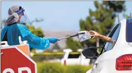  ?? Allen J. Schaben Los Angeles Times ?? CUROGRAM SPECIALIST Mari Cruz retrieves a completed coronaviru­s test from a motorist Monday at the Orange County Great Park in Irvine.