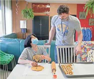  ?? BARBARA J. PERENIC/COLUMBUS DISPATCH ?? Yuka Takagi, 21, left, laughs as she cuts out bone-shaped dog treats from dough assisted by interventi­on specialist Shane Natalie at Gahanna Lincoln High School. Students in the school’s special education program are part of a business making and selling dog treats.