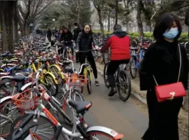  ?? ANDY WONG, THE ASSOCIATED PRESS ?? People try to pedal through a sidewalk crowded with bicycles from bike-sharing companies Ofo, Mobike and Bluegogo, near a bus stand in Beijing.