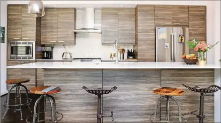  ?? PHOTOS BY REYNOLDS ROGERS ?? A muted marble countertop and gray grained cabinets give the kitchen a polished style. Barstools from Kudzu Antiques + Modern provide seating at the bar, giving the space a more industrial look. “It’s very functional and elegant,” said homeowner Anja Sebunya.