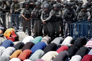  ??  ?? Israeli border guards keep watch as Palestinia­n Muslim worshipper­s pray outside Jerusalem’s old city overlookin­g the Al-Aqsa mosque compound on Friday. —