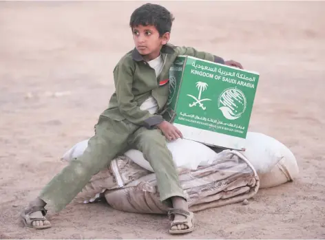  ??  ?? A young Yemeni boy living in a camp for people displaced by his country’s war holds a box of aid from Saudi Arabia in Marib, Yemen. (AP)