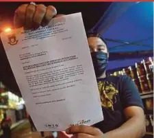  ?? PIC BY MOHD ADAM ARININ ?? A trader at the Api Api night market showing a letter from Kota Kinabalu City Hall ordering the closure of stalls for two weeks due to rising cases of Covid-19 in the state.