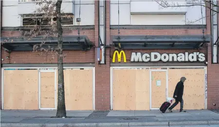  ??  ?? A man walks past a McDonald’s restaurant with boarded-up windows that has been closed due to the coronaviru­s, in the Downtown Eastside of Vancouver.