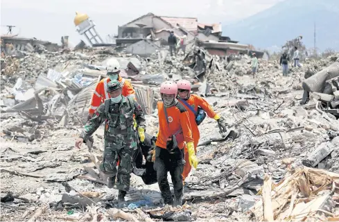  ??  ?? STILL PULLING OUT REMAINS: Rescue workers and a soldier remove a victim of last week’s earthquake in the Balaroa neighbourh­ood in Palu yesterday.