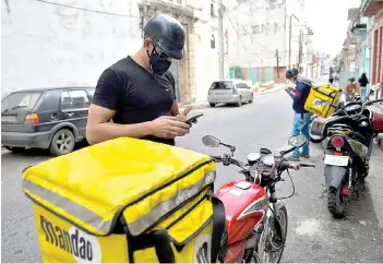  ??  ?? A Cuban delivery man from “Mandao”, a food and product delivery service, manages delivery requests through his cell phone in Havana.