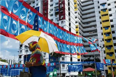  ?? — Bernama ?? Shades of blue: A woman walking past flags of political parties ahead of the coming election.
