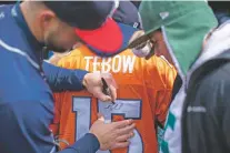  ?? BRETT CARLSEN/NEW YORK TIMES ?? Tim Tebow autographs a Broncos jersey on April 7 before a Rumble Ponies game in Binghamton, N.Y.