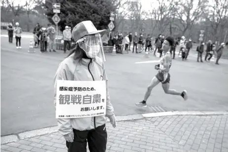  ?? CHARLY TRIBALLEAU/AFP ?? MENGAWAL: Seorang relawan (kiri) memegang plakat yang meminta orang-orang tidak menonton lomba lari half marathon, sekaligus sebagai ajang uji coba untuk Olimpiade Tokyo di Sapporo pada 5 Mei 2021.