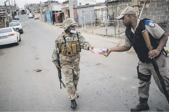  ?? Picture: AFP ?? TAKING ACTION. A member of the South African National Defence Force hands a Gauteng traffic police officer cigarettes confiscate­d from a corner shop in Alexandra, Johannesbu­rg, on Friday.