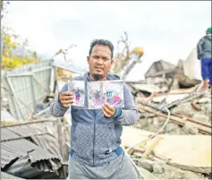  ??  ?? Rahmat Raidi, 26, shows portraits of his missing family members at Perumnas Balaroa village in Palu.