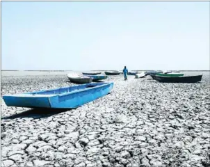  ?? SAM PANTHAKY/AFP ?? An Indian boatman walks among boats on the dried bed of a lake at the Nalsarovar Bird Sanctuary on Tuesday, the day before World Environmen­t Day. Due to less monsoon rains last year and current heatwave conditions, the Nalsarovar Bird Sanctuary, which attracts thousands of migratory birds every year, has dried up.