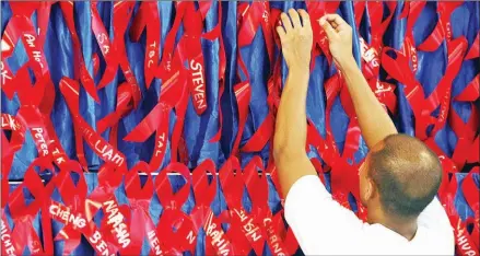  ?? ROSLAN RAHMAN/AFP ?? A volunteer pins ribbons bearing the names of people who died of HIV/AIDS during the AIDS Candleligh­t Memorial in Singapore.