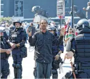  ??  ?? A man live streams video Sunday as he is detained by Charlotte-Mecklenbur­g police outside Bank of America Stadium, where people were protesting, in Charlotte, N.C. The man was detained for items contained in his backpack.