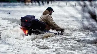  ?? Ted S. Warren / Associated Press ?? A man holds on to his all-terrain vehicle Friday as he it is swept off a road by floodwater­s from the Chehalis River near Centralia, Wash. He was able to swim to safety.