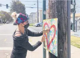  ?? JANIE MCCAULEY/AP ?? Artist Deirdre Freeman hangs her artwork on a telephone pole April 13 in Alameda, California. Freeman has hung over 120 pieces of artwork on poles around the city.