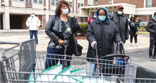 ?? TYLER LARIVIERE/SUN-TIMES ?? Helen Chambers (left) and Rosemary Coleman, president of the CHA’s local advisory council, stand behind a cart full of masks and gloves that’s being donated to the seniors at Patrick Sullivan Senior Apartments.