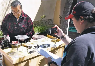  ?? CLYDE MUELLER/THE NEW MEXICAN ?? Monica Lovato, right, a member of the Palace of the Governors’ portal artisan committee, photograph­s Eddie Chavez of Santo Domingo Pueblo as he works Thursday to earn certificat­ion that he creates the silver products he sells under the portal. Some...