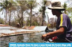  ?? Reuters ?? SREKOR, Cambodia: Kheun Fut steers a canoe through this flooded village while his father Noy Fut salvages metal sheets from the roof of his former house on May 15, 2018. —