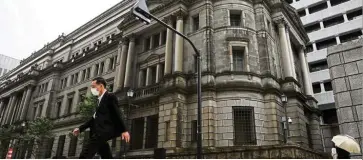  ??  ?? Helping hand: A man wearing a protective mask walks past the headquarte­rs of the BOJ. The central bank has pledged cooperatio­n to get funds to struggling businesses.