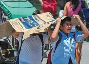  ?? ?? students use a cardboard to protect themselves from the sun during a hot day in Manila.