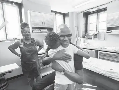  ?? KENNETH K. LAM/BALTIMORE SUN ?? Artist Mark Bradford, center, gets a hug from Caelib Brooks, 11, as printer Sylvia Butler looks on at Greenmount West Power Press. The community workshop teaches kids how to do silk screening.