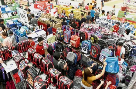  ??  ?? New school year beckons: Parents and their kids shopping for shoes and school bags at AEON Cheras Selatan. Right: A shop in Kepong selling white school shirts for RM1 is packed with parents and children.