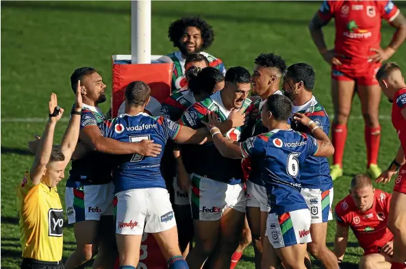  ?? GETTY IMAGES ?? The Warriors mob Jamayne Taunoa-brown, centre, after his early try set up their shutout win over the Dragons.