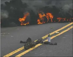  ?? The Associated Press ?? CONTINUOUS ERUPTIONS: Lava burns across a road as an offering to the volcano goddess lies in the foreground in the Leilani Estates subdivisio­n near Pahoa, Hawaii, on Saturday. Glowing plumes of lava have shot hundreds of feet into the air at points,...