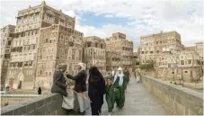  ?? — AFP ?? Two Yemeni men sit and talk by the ledge of a bridge as another woman and two girls pass by next to them, with the Unesco-listed buildings of the old city of Sanaa in background behind them, on Wednesday.