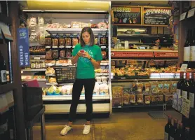  ?? Lea Suzuki / The Chronicle 2014 ?? Instacart personal shopper Sydney Hollingswo­rth checks a customer’s order on her phone while picking items up in Bi-Rite Market in San Francisco.