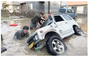  ?? — AFP ?? Team work: Residents trying to upright a vehicle stuck in a flood hit area in Kurashiki, Okayama prefecture.