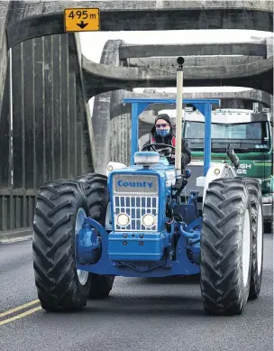  ?? PHOTOS: JOHN COSGROVE ?? On the road again . . . Brendon Storer, a teacher aide at Stirling School, drives his 1974 Ford Country 754 tractor over the Balclutha bridge yesterday morning, on his way south to attend the 32nd annual Crank Up at Edendale, north of Invercargi­ll.