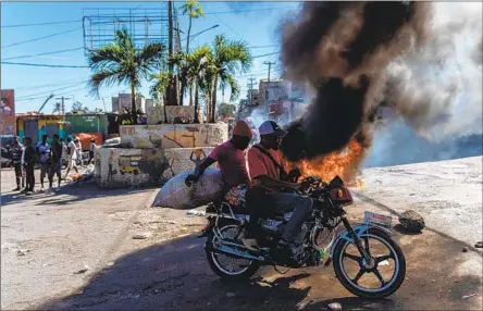  ?? Richard Pierrin AFP/Getty Images ?? PEOPLE pass tires being burned during a demonstrat­ion in Port-au-Prince, Haiti, on Jan. 26, a day after a gang killed six police officers.