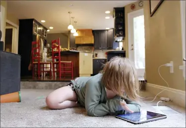  ?? SARA CLINE- ASSOCIATED PRESS ?? Lizzie Dale sprawls on the floor to play games on an iPad as her siblings work on school work in the kitchen behind her in their home in Lake Oswego, Ore., Oct. 30. In Oregon, one of only a handful of states that has required a partial or statewide closure of schools in the midst of the COVID-19 pandemic, parents in favor of their children returning to in-person learning have voiced their concerns and grievances using social media, petitions, letters to state officials, emotional testimonie­s at virtual school board meetings and on the steps of the state’s Capitol.