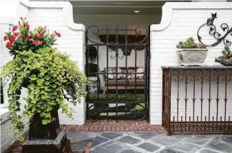  ??  ?? A gate in the fountain garden off the living room leads to a covered seating area in a portico. The ironwork and marble buffet is from Joyce Horn Antiques.