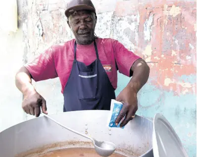  ?? KENYON HEMANS/ PHOTOGRAPH­ER ?? A popular soup vendor from Allman Town adds salt to his pot of red peas soup on July 13.