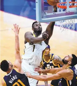  ?? GERALD HERBERT AP ?? Pelicans forward Zion Williamson, who had 26 points and 10 rebounds, goes to the basket over Jazz forward Georges Niang (left) and center Rudy Gobert.