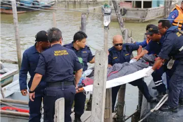  ??  ?? Maritime personnel carry one of the rescued crewmen to the Pantai Leka fishermen’s jetty. — Bernama photo
