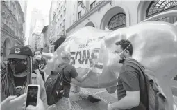  ?? ANDRE PENNER/AP ?? Activists paste the Portuguese word “hungry” on the Golden Bull on Nov. 17 outside the Brazilian B3 Stock Exchange in Sao Paulo, Brazil.