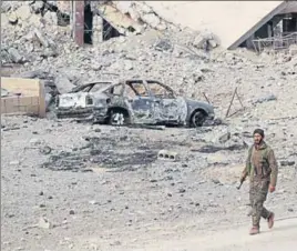  ?? AFP ?? A member of Syria's Arab Shaytat tribe who joined a Kurdish-led alliance fighting the Islamic State group in Syria, walks past the debris of a bombed car in the Syrian village of Baghouz.